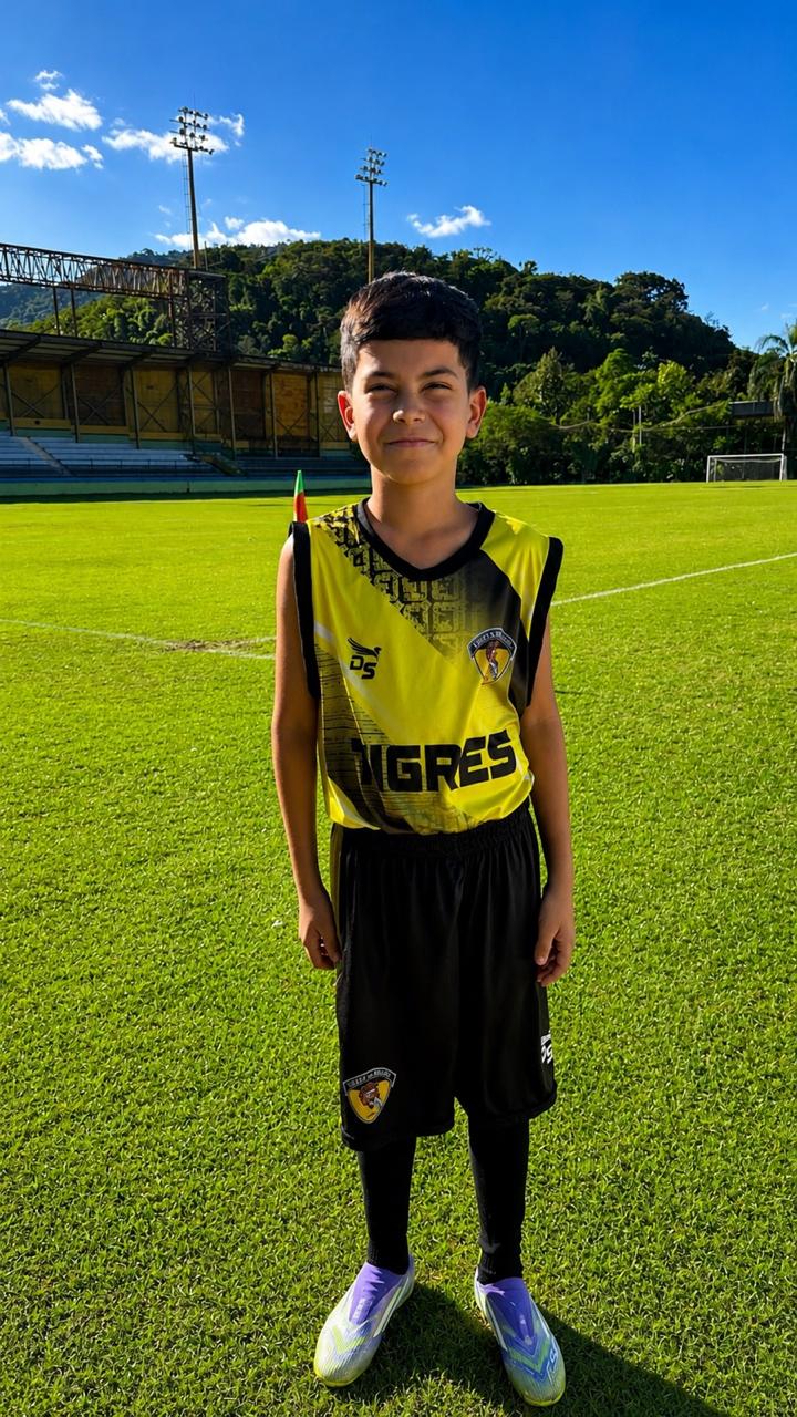 Hugo de uniforme do Tigres, de corpo inteiro no gramado sob o céu azul