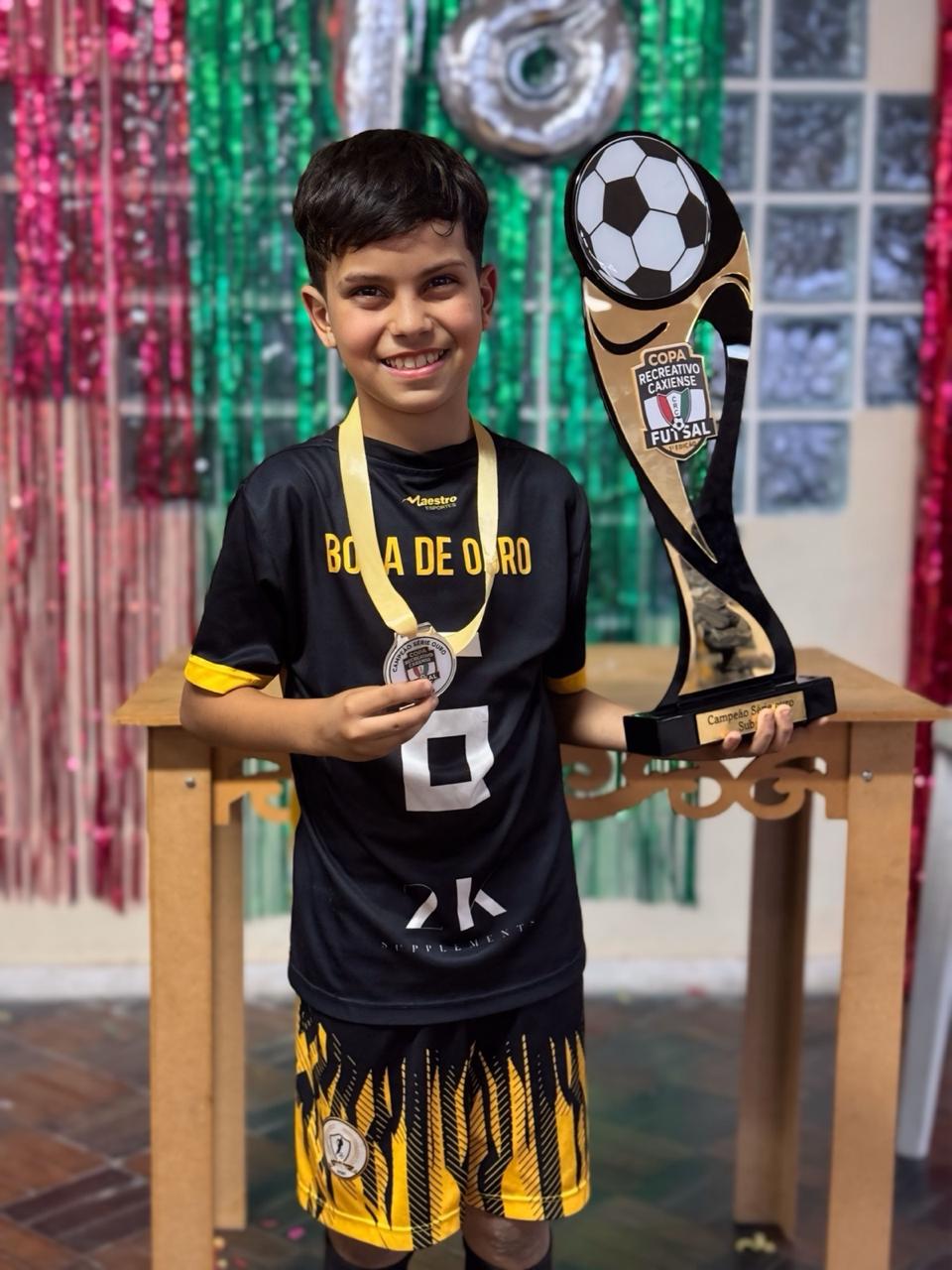 Hugo sorrindo com a medalha no pescoço e o troféu da Copa Recreativo Caxiense nas mãos